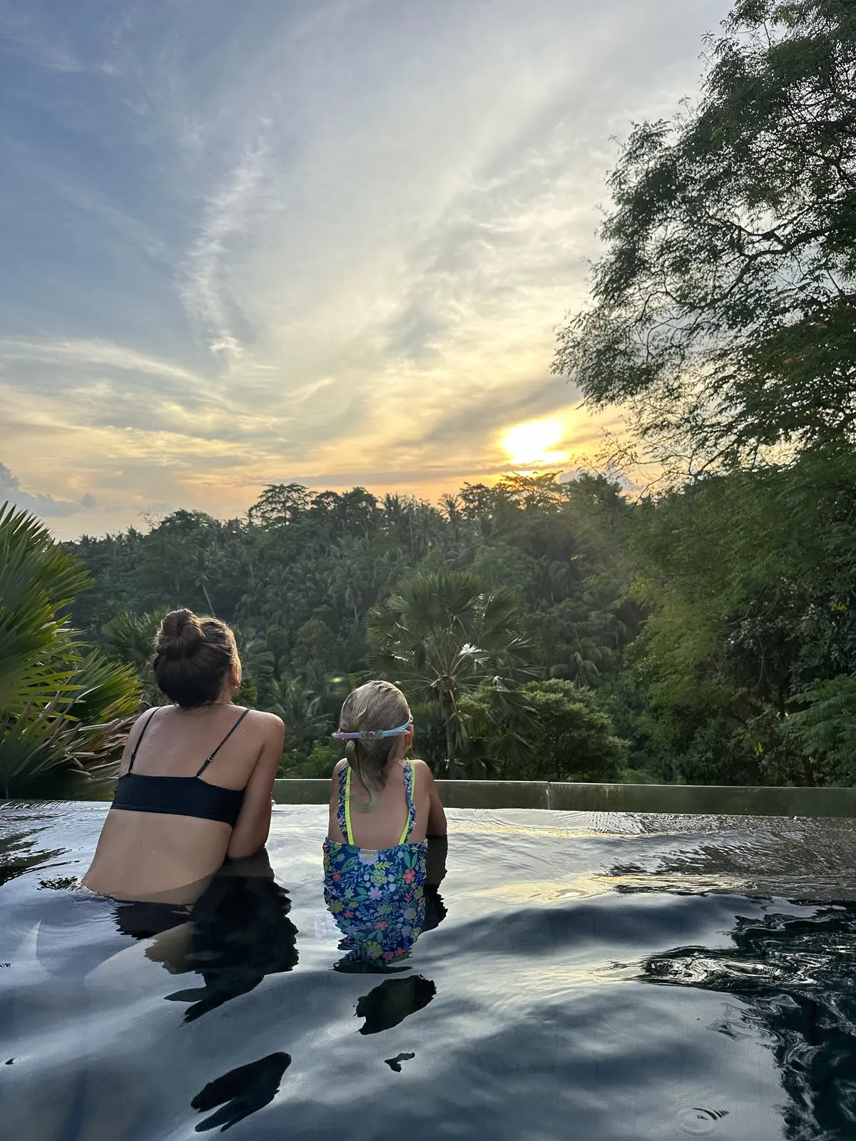 Kailah and our daughter in an infinity pool looking out over the jungle at sunset in Bali