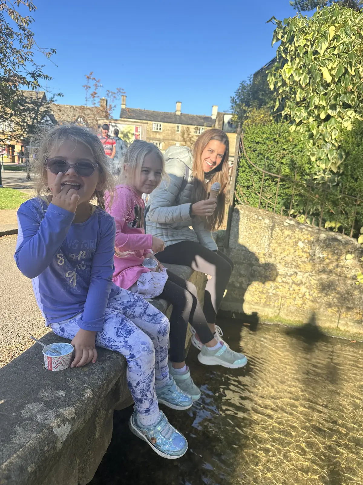 Kailah and our two daughters eating ice cream beside a shallow stream in a Cotswolds village