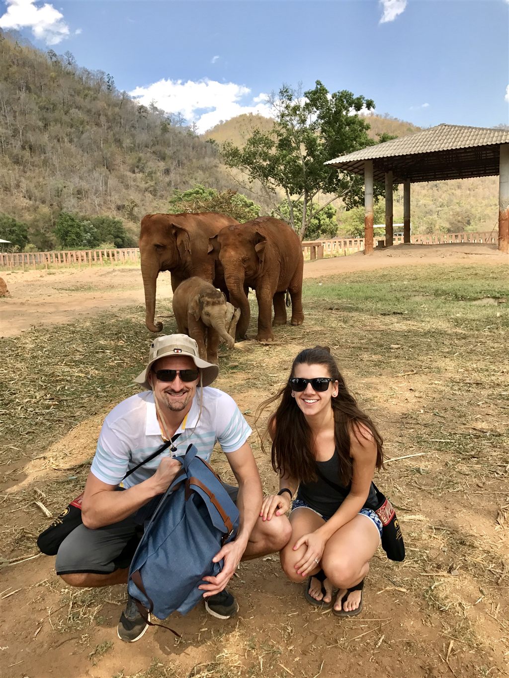 Kyle and Kailah crouching near a family of elephants at a sanctuary in northern Thailand